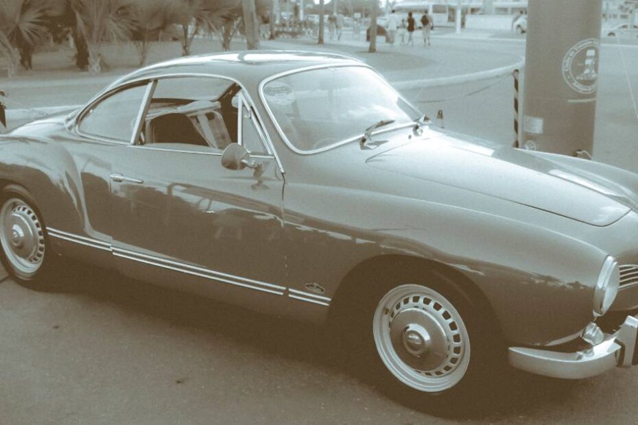 Here's a black-and-white photo of a classic VW Karmann Ghia parked off the side of the road. You can see people walking in the background.