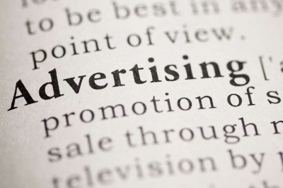 The word advertising is in bold lettering inside of a dictionary. You can see part of the definition of advertising in the image.