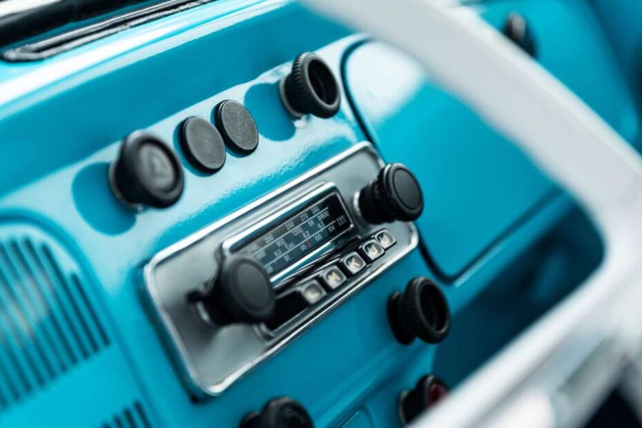 A vintage VW Beetle's radio and dashboard is in focus. The car's entire interior is light blue with black finishes.